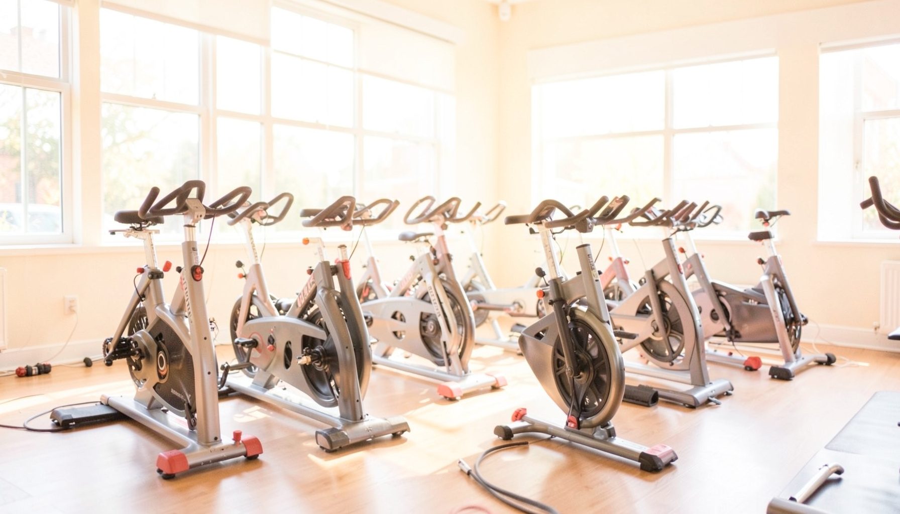 A bright, airy indoor cycling studio with stationary bikes lined up, soft natural light streaming through large windows, warm and energetic atmosphere