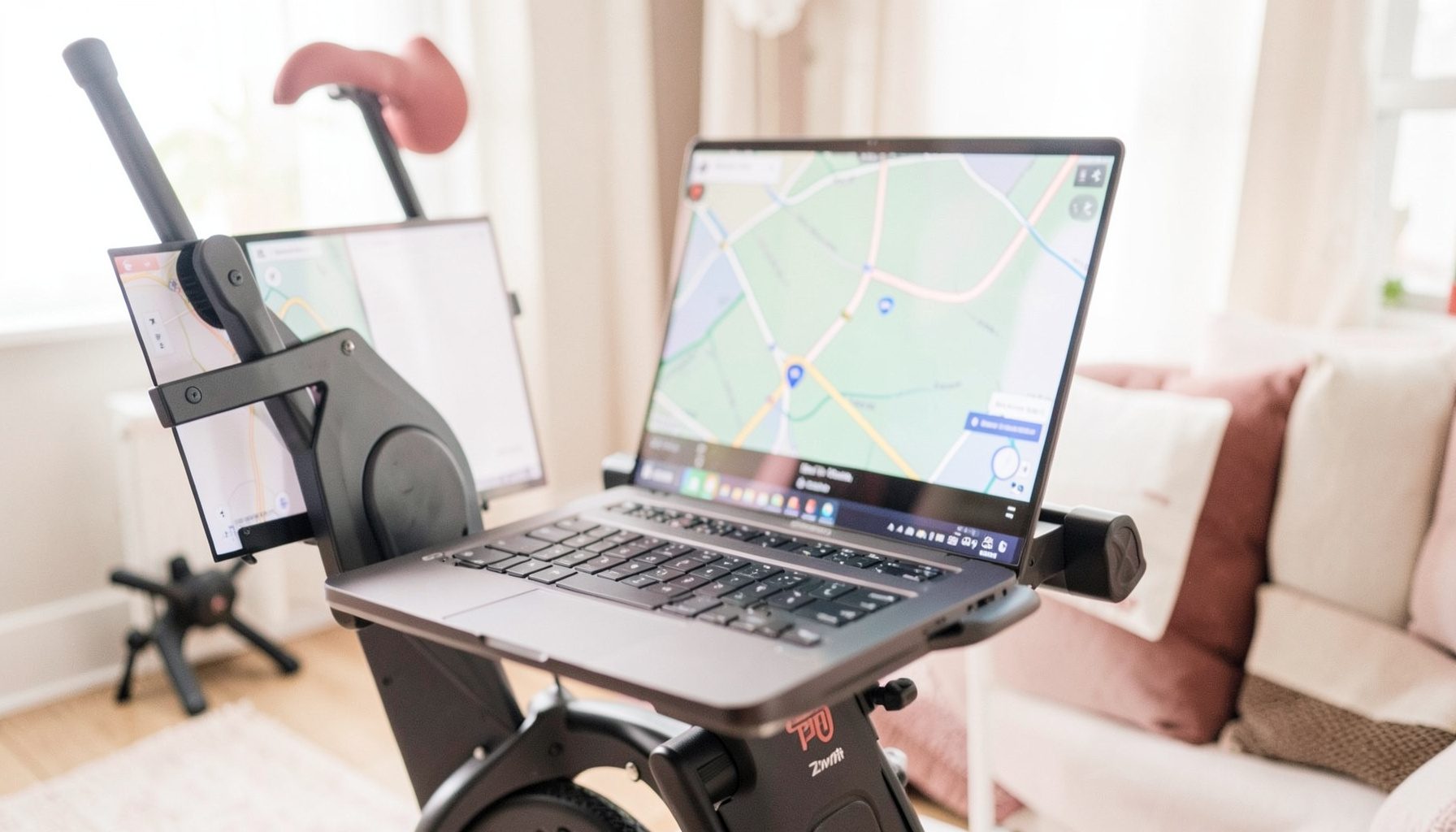 Close-up of a bike trainer setup with a laptop running Zwift, colorful course map on screen, cozy home training corner